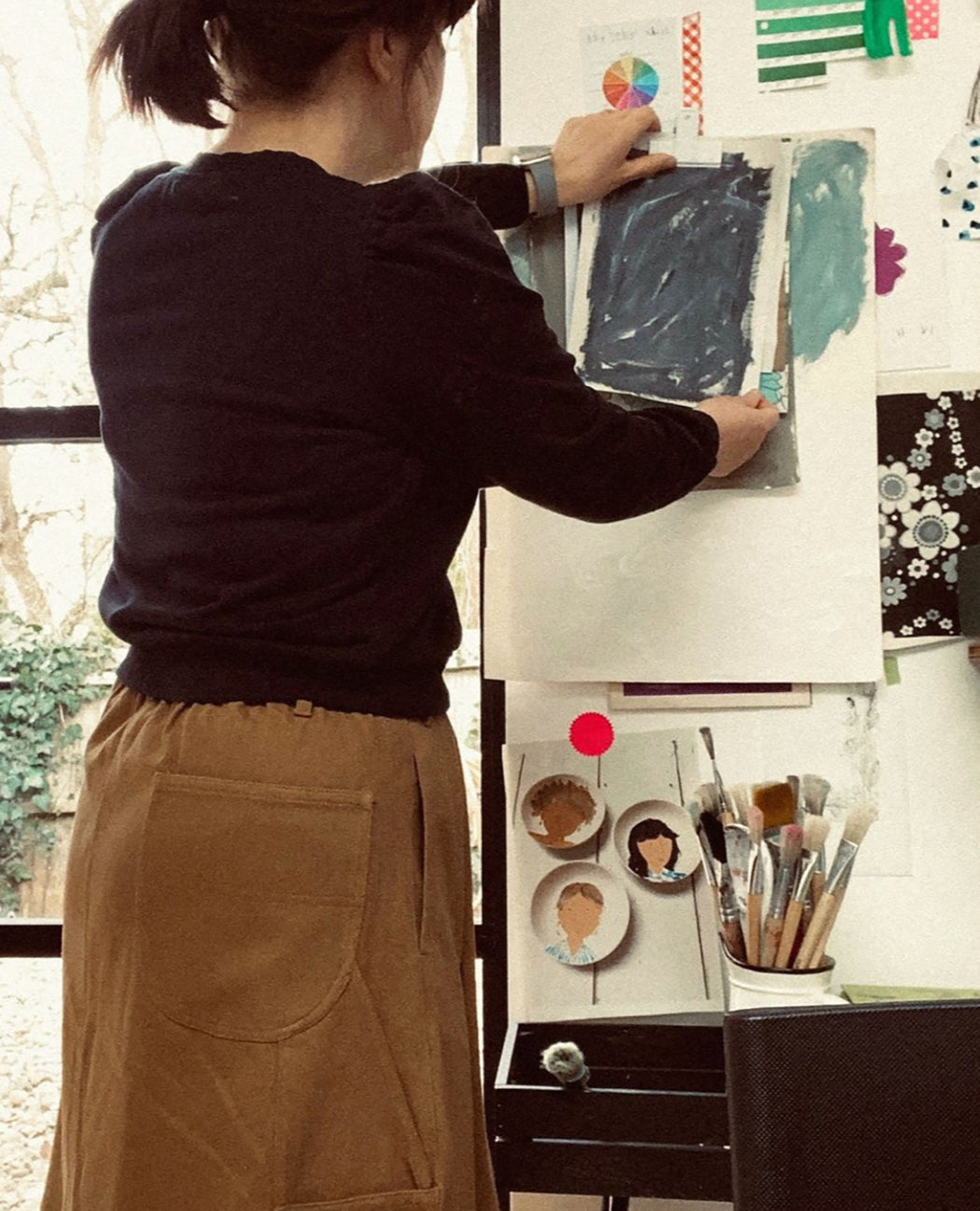 Person working on a painting in an art studio with various art supplies and decorations.
